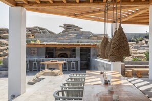 Ein Sitzbereich im Freien mit einer Holz-Pergola, Steinmauern und hängenden, gewebten Lampen.