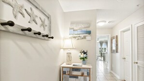 Ein Flur mit einer Konsole, Wanddekoration mit Meeressternen, einer Lampe und einer Vase mit Blumen.
