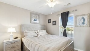 Ein Schlafzimmer mit Bett, Nachttisch, Lampe, Deckenventilator und Bildern an den Wänden.