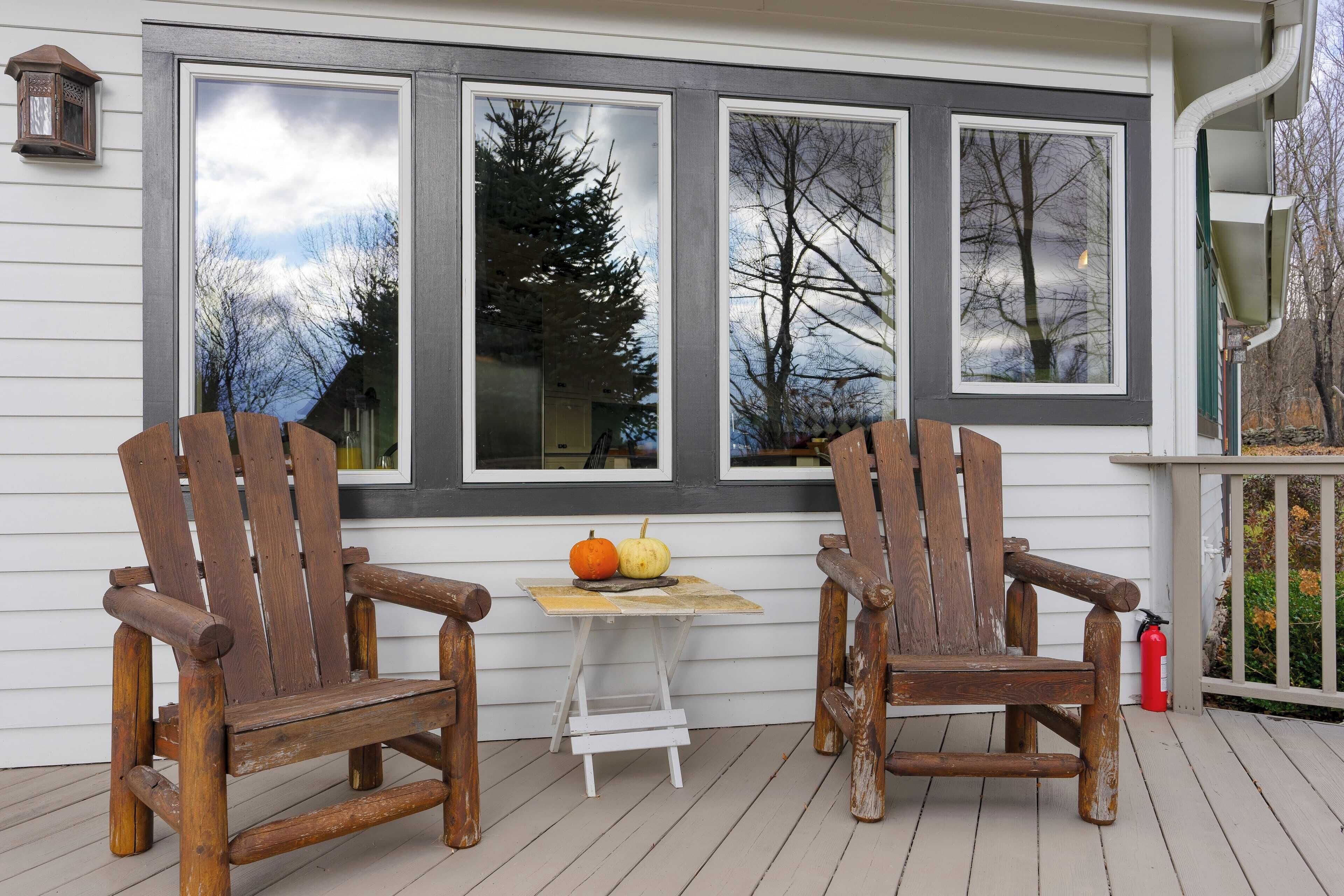 A wooden deck with two Adirondack chairs and a small table with pumpkins.