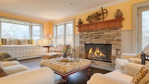 A cozy living room with a stone fireplace, large windows, and comfortable seating.