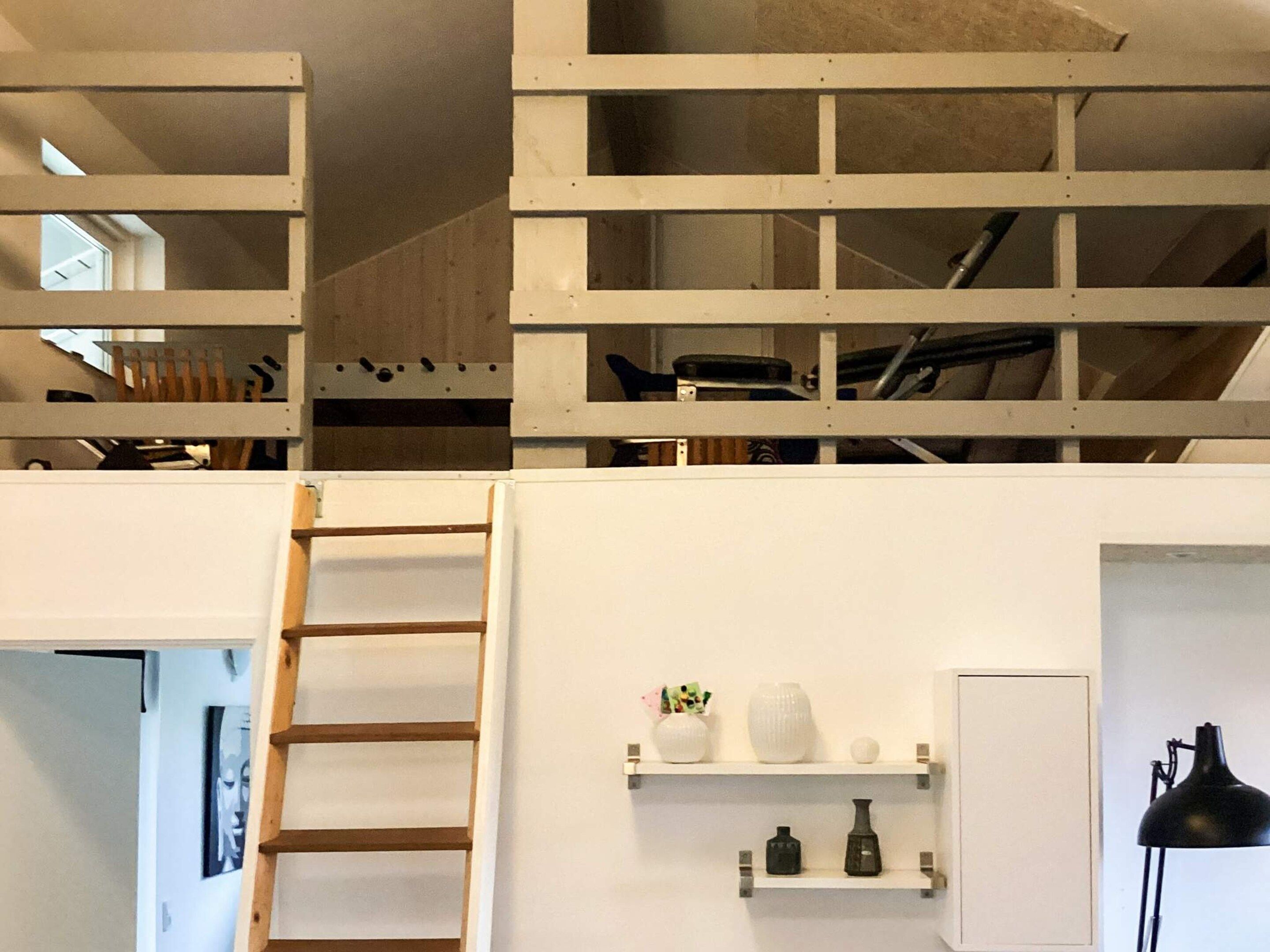 A loft-style room with a wooden ladder, white walls, and shelves with decorative items.