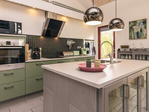 A modern kitchen with green cabinets, a Bosch oven, a microwave, and a large island with a pink bowl. - 4 Star Holiday Home in Vaeggerlose (Vaeggerlose)