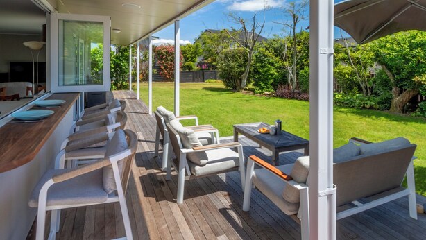 Une terrasse extérieure couverte avec une plateforme en bois, des meubles blancs et une vue sur un jardin bien entretenu.