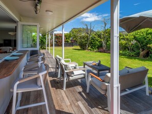 Eine überdachte Terrasse im Freien mit Holzdeck, weißen Möbeln und Blick auf einen gepflegten Garten.