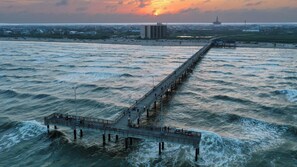 A pier extending into the sea with a building in the background. - Sailfish at Trout Street Waterfront Escape + Patio Walk to Port A Nightlife (Port Aransas)