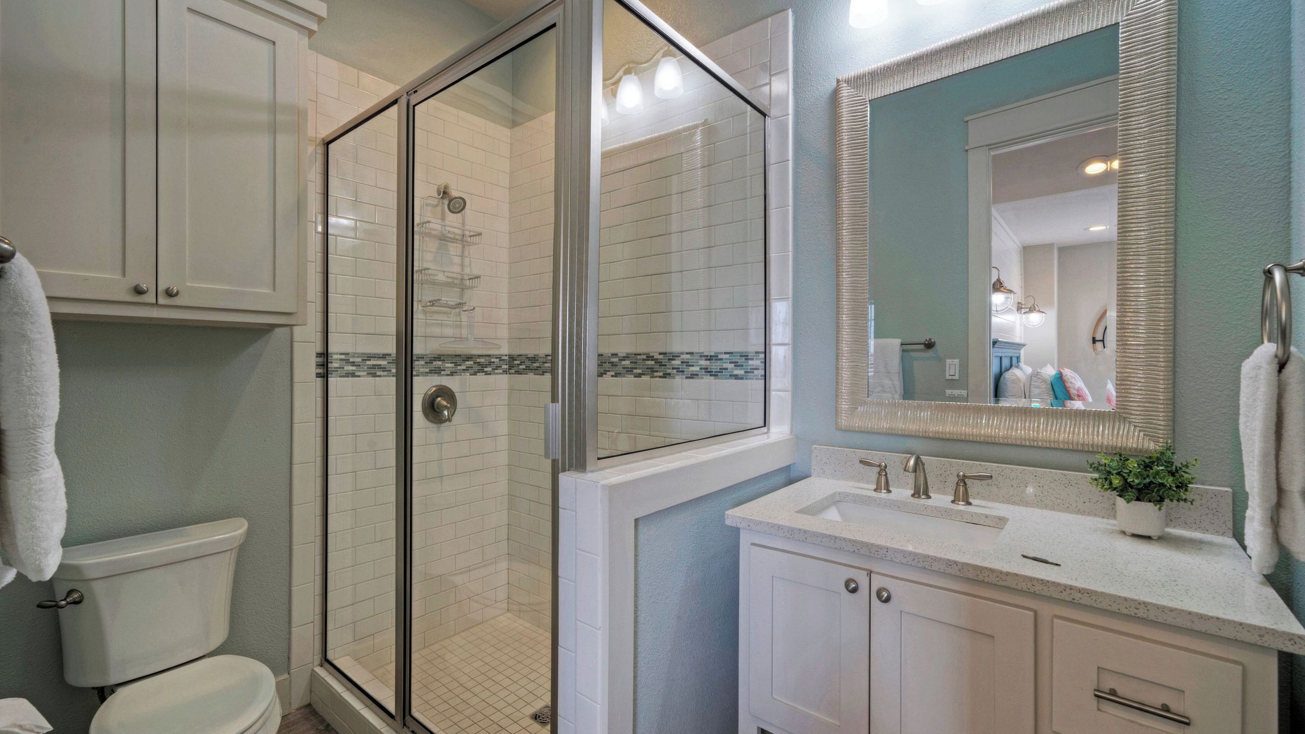 A bathroom with a glass-enclosed shower, a white toilet, a sink with a mirror, and cabinets.