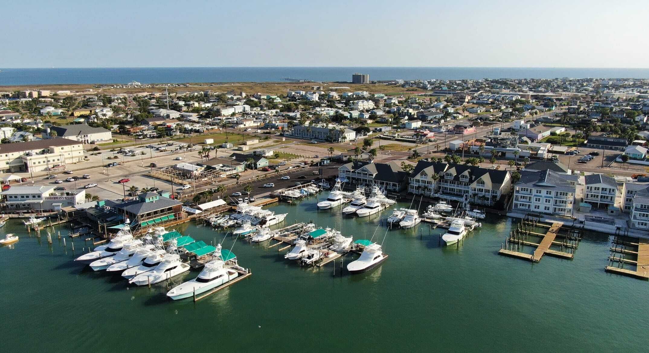 Un puerto deportivo con numerosas embarcaciones amarradas, rodeado de edificios residenciales y una vista despejada del océano.