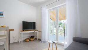 A modern living room with a flat-screen TV on a white console table, a grey sofa, and a small round table with a remote control. - Attractive Apartment With Garden (Porec)