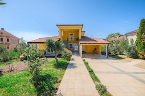 A yellow house with a tiled roof, a covered porch, and a garden with a paved walkway. - Attractive Apartment With Garden (Porec)