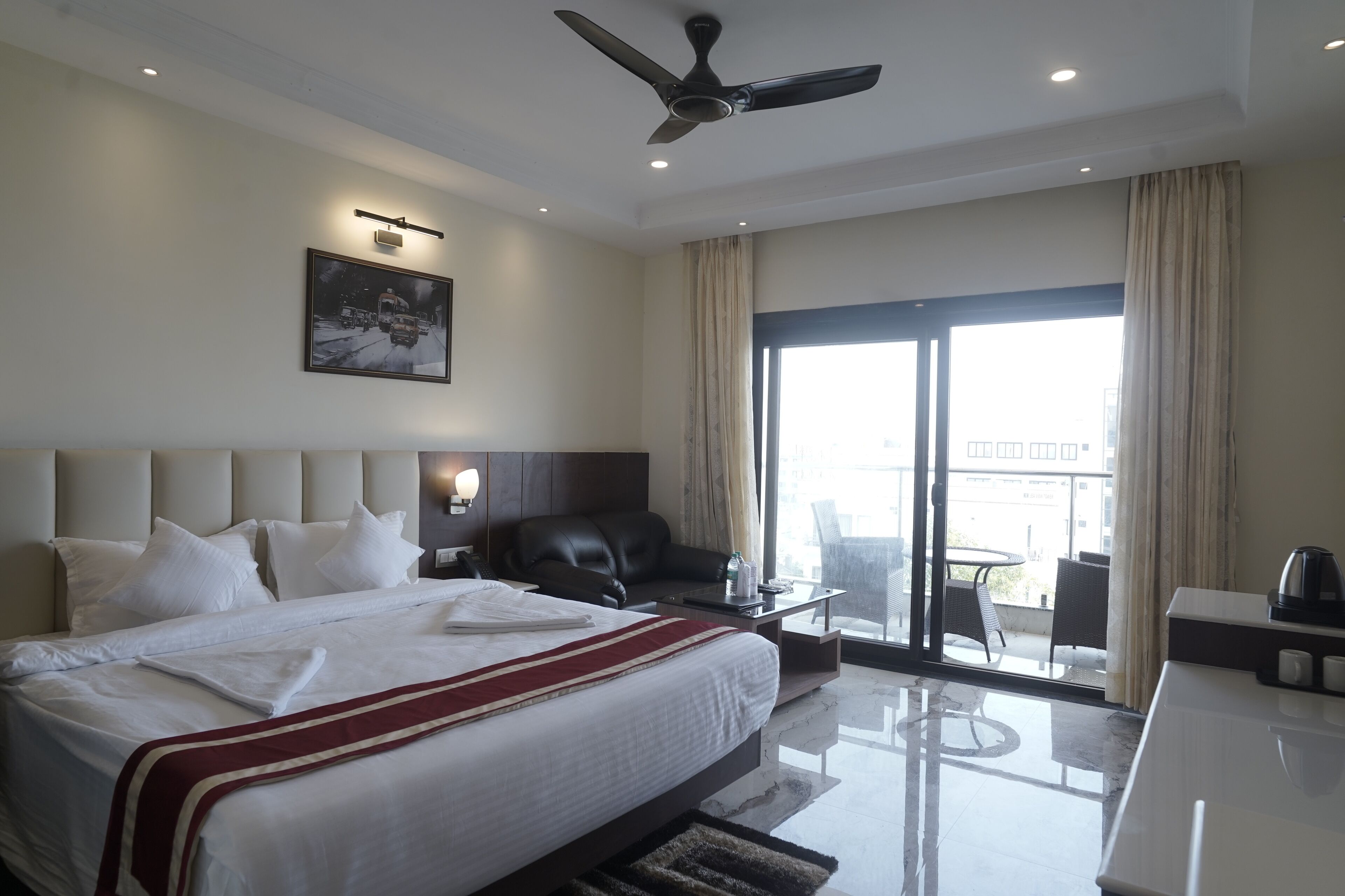 A hotel room with a large bed, a desk, a chair, a ceiling fan, and a balcony with a view.