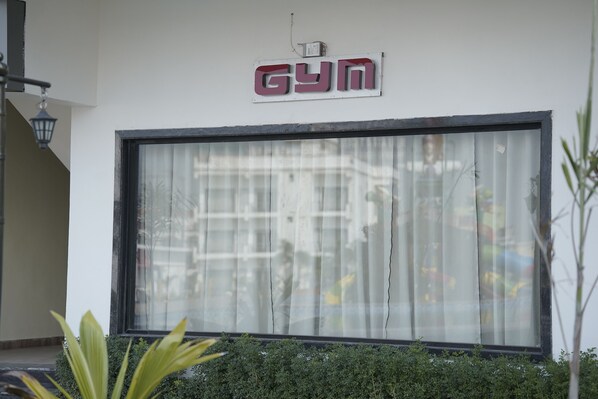 A gym sign on a building with a large window and a small garden area in front.