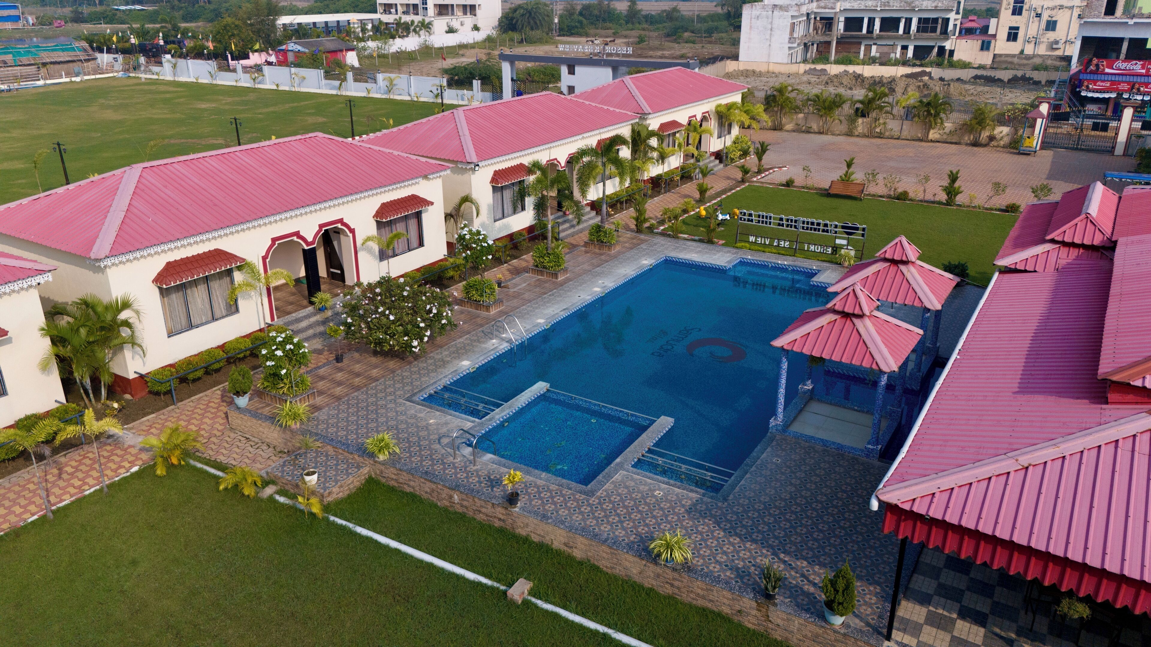A hotel with a swimming pool, multiple buildings with red roofs, and a well-maintained lawn.