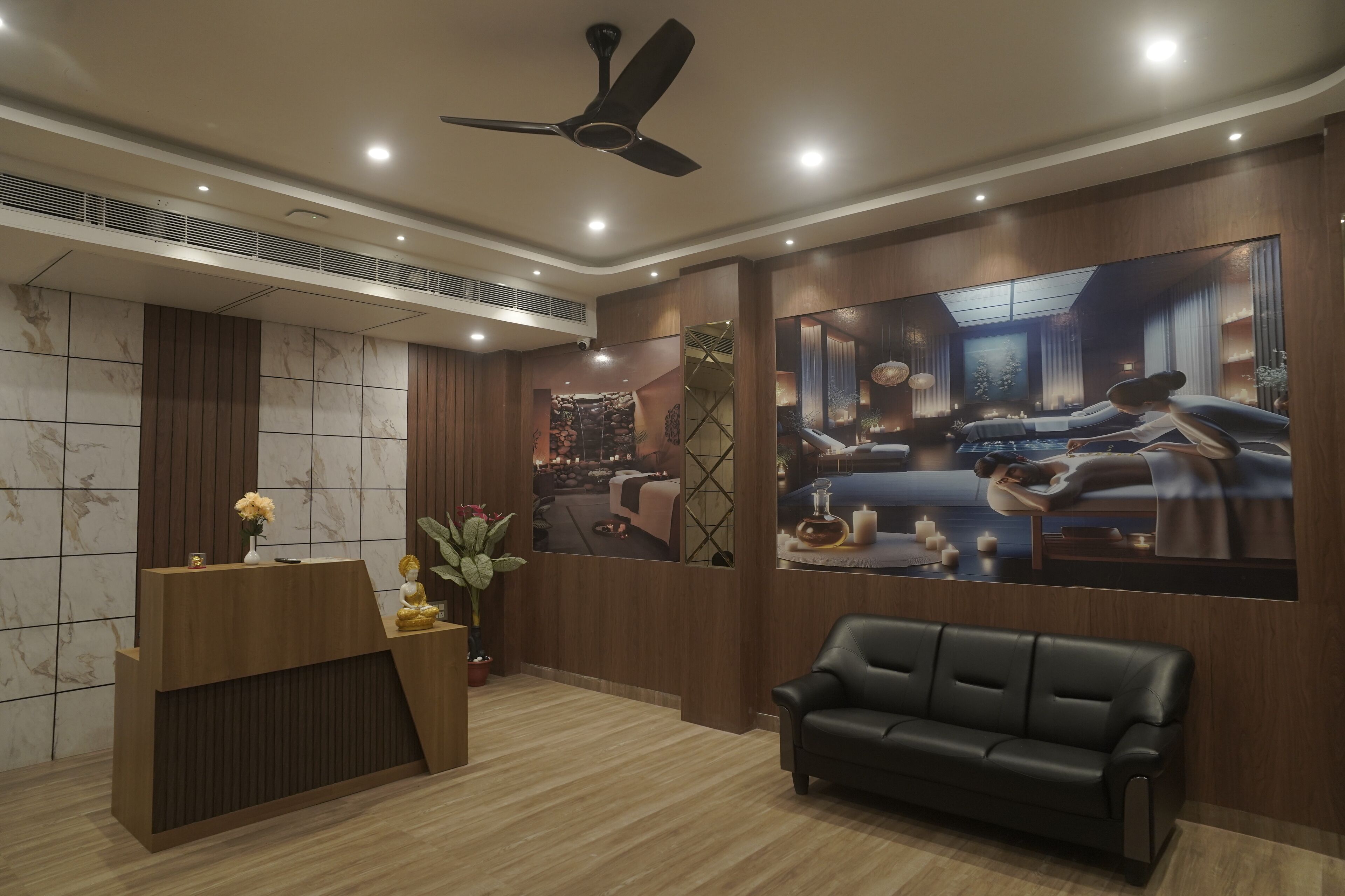 A reception area with a wooden desk, a black leather sofa, and a large framed picture of a bedroom.