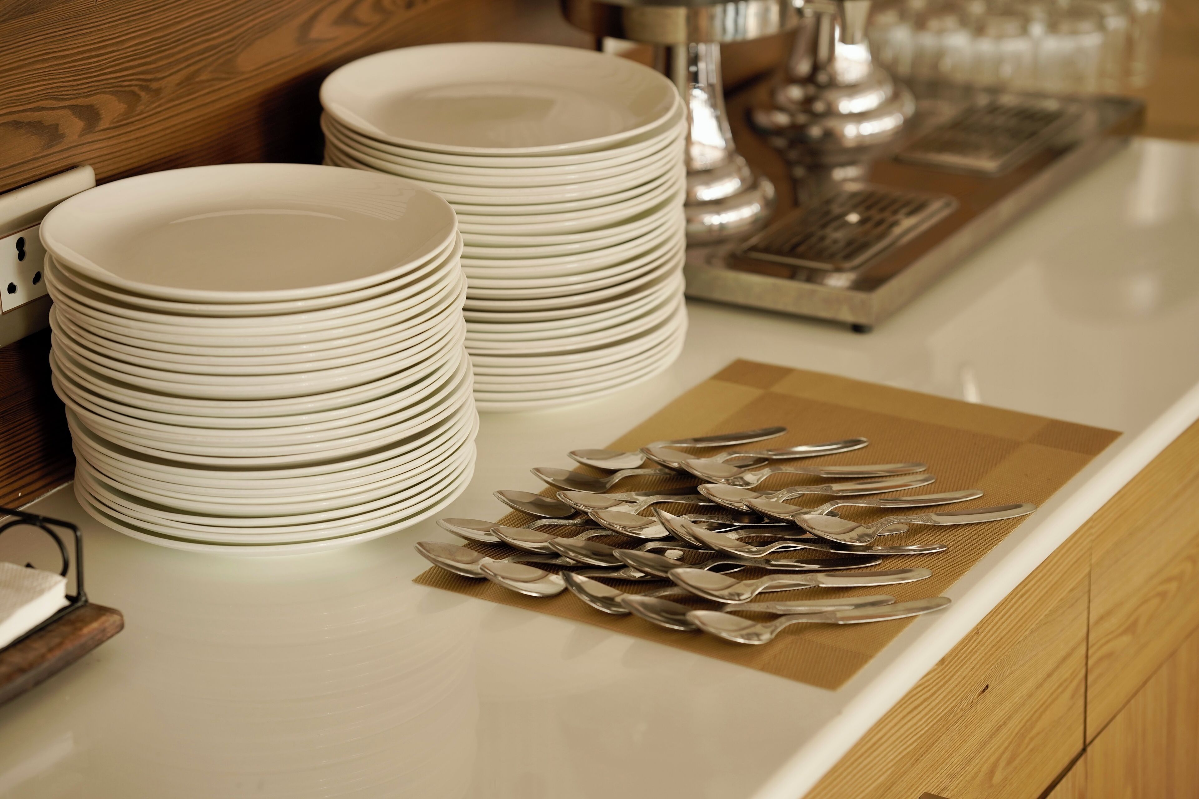 Stacks of white plates and silverware on a kitchen counter.