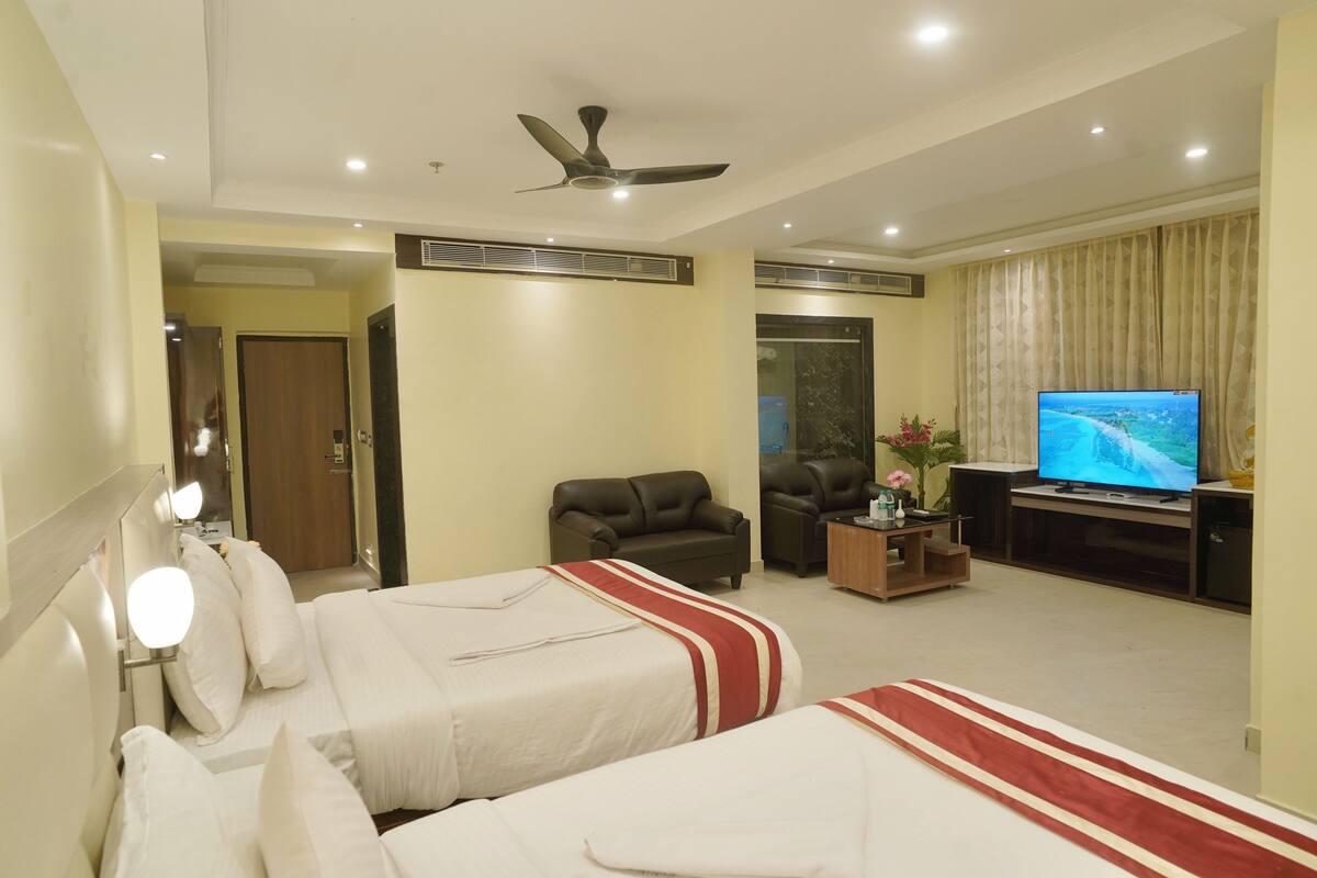 Habitación de hotel con dos camas, televisión, ventilador de techo y zona de estar.