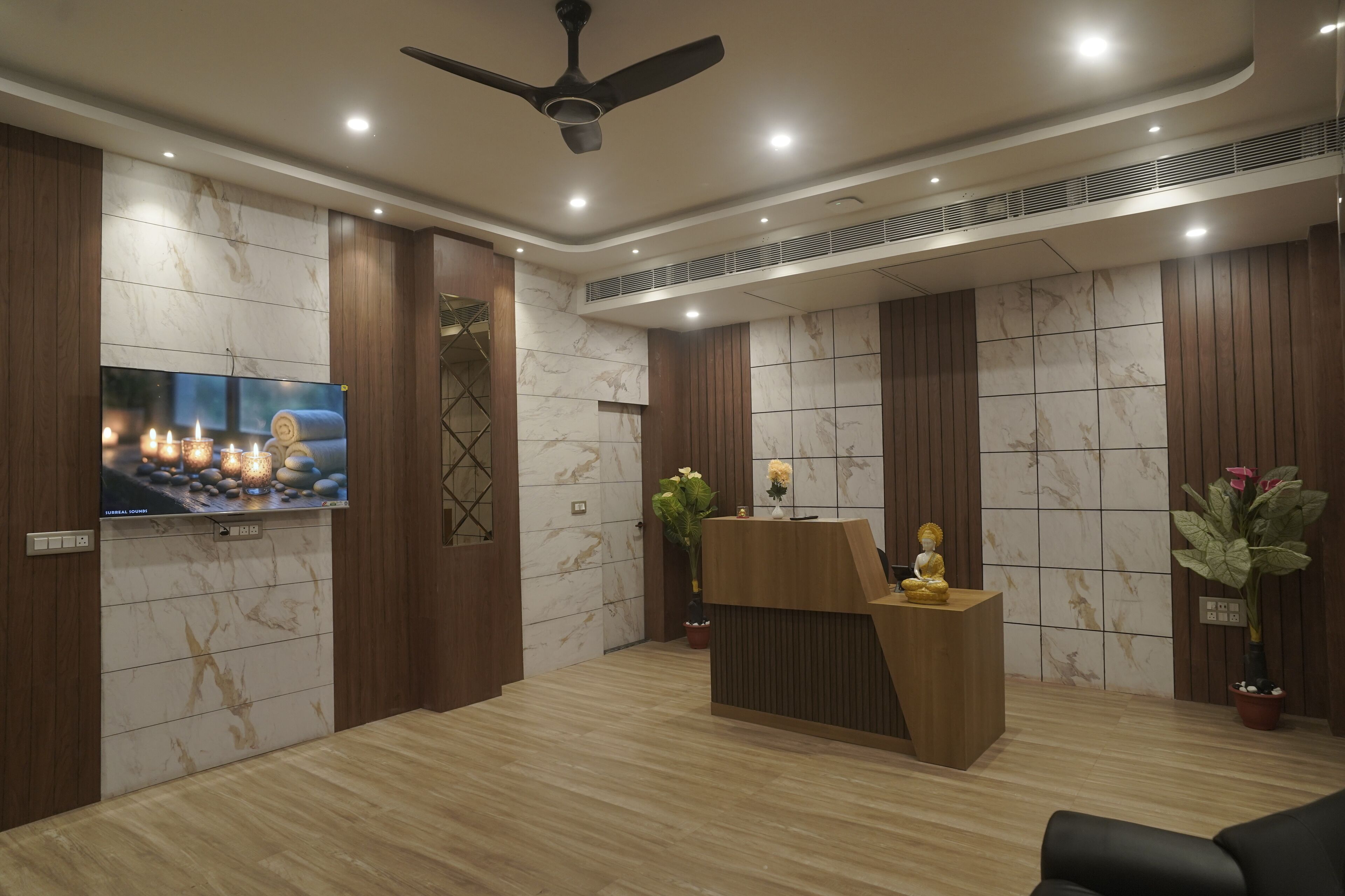 A reception area with a wooden reception desk, a television mounted on the wall, and a ceiling fan.