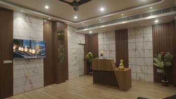 A reception area with a wooden reception desk, a television mounted on the wall, and a ceiling fan.