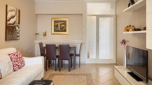 A living room with a white sofa, a dining table with chairs, a TV, and artwork on the walls. - Apartment in Porec Near Spadici Beach (Porec)