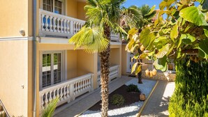 A two-story building with a balcony, a palm tree, and a garden area with gravel and plants. - Apartment in Porec Near Spadici Beach (Porec)