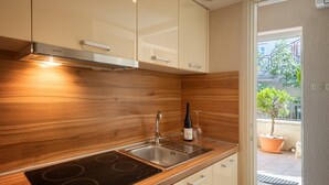 A modern kitchen with a wooden backsplash, stainless steel sink, and a built-in induction cooktop. - Apartment in Porec Near Spadici Beach (Porec)