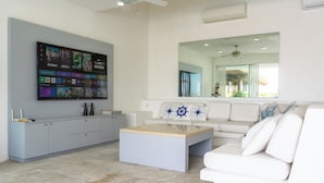 A modern living room with a flat-screen TV, a white sofa, a coffee table, and a large mirror. - Villa Majum Ocean View Acapulco 5 BDR (Acapulco)
