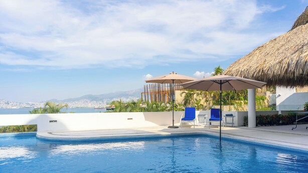 A swimming pool with a view of the city, a thatched roof structure, and lounge chairs. - Villa Majum Ocean View Acapulco 5 BDR (Acapulco)