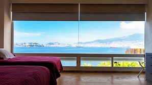 A bedroom with two beds, a large window with a city and sea view, and a wooden chair. - Villa Majum Ocean View Acapulco 5 BDR (Acapulco)
