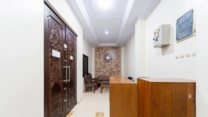 A reception area with a wooden desk, a clock on the wall, and a patterned wall behind the desk. - Tebet Utara Suites (Jakarta)