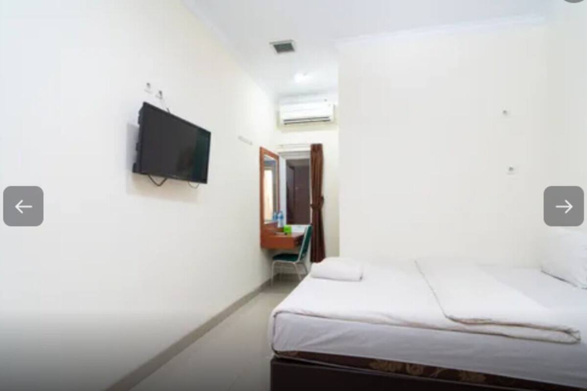 A small, clean room with a bed, a TV mounted on the wall, and a mirror above a desk.