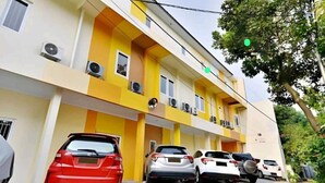 A multi-story building with a yellow facade, air conditioning units, and a parking area with several cars. - Tebet Utara Suites (Jakarta)