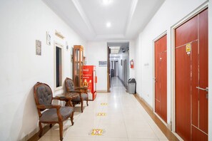 A hotel corridor with wooden chairs, a Coca-Cola refrigerator, and red doors. - Tebet Utara Suites (Jakarta)