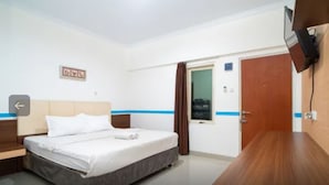 A hotel room with a bed, a wooden nightstand, a flat-screen TV mounted on the wall, and a door with a window. - Tebet Utara Suites (Jakarta)