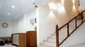A spacious living area with a wooden reception desk, a staircase with wooden railings, and a white wall with a clock. - Tebet Utara Suites (Jakarta)