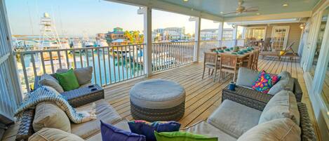 A covered outdoor seating area with wicker furniture, cushions, and a view of the marina.