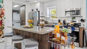 A modern kitchen with a central island, stainless steel appliances, and bar stools. - Heated Pool, Tiki Hut, Huge Yard, Bar, Walk 2 Ave (Delray Beach)