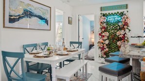 A dining area with a white table set for four, teal chairs, and a floral wall decoration with a 'WELCOME' sign. - Heated Pool, Tiki Hut, Huge Yard, Bar, Walk 2 Ave (Delray Beach)