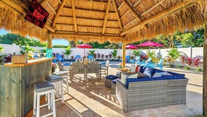 An outdoor patio area with a thatched roof, wicker furniture, a bar, and a pool. - Heated Pool, Tiki Hut, Huge Yard, Bar, Walk 2 Ave (Delray Beach)