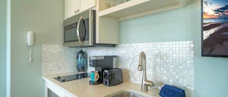 A compact kitchen with a microwave, toaster, and coffee maker on the counter, a sink, and a blue towel.