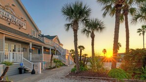 A beachfront building with a bar and grill, palm trees, and a sunset. - Dolphin at Trout Street Queen Suite w/ Kitchenette Marina-front + Patio (Port Aransas)