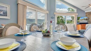 A dining area with a long table set for six, large windows, and a stone wall. - Hook & Paddle - Luxury home on SML with kayaks and private dock. (Huddleston)