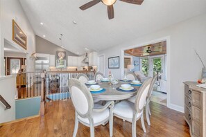 Un coin repas avec une table ronde, des chaises blanches et un ventilateur de plafond.