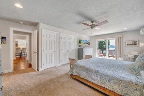 Une chambre avec un grand lit, un ventilateur de plafond et un téléviseur posé sur une commode. Une porte donne sur un balcon équipé d’une chaise et d’une table.