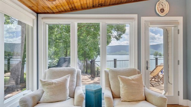 A cozy room with two armchairs, a blue side table, and large windows offering a view of a lake and trees. - Hook & Paddle - Luxury home on SML with kayaks and private dock. (Huddleston)
