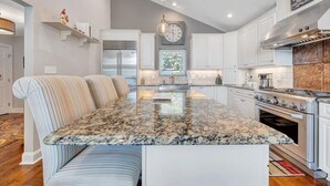 A modern kitchen with a central island, stainless steel appliances, and a striped bench. - Hook & Paddle - Luxury home on SML with kayaks and private dock. (Huddleston)