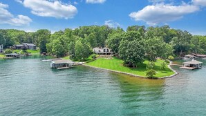 A lakeside property with a large house surrounded by lush greenery, connected to the shore by a dock. - Hook & Paddle - Luxury home on SML with kayaks and private dock. (Huddleston)