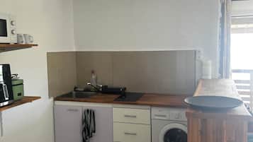 Cocina compacta con microondas, lavaplatos y lavadora. Tiene una encimera de madera y un pequeño cubo de basura.