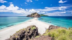 Een strand met helder turquoise water, een klein bootje en een rotsachtige landtong.