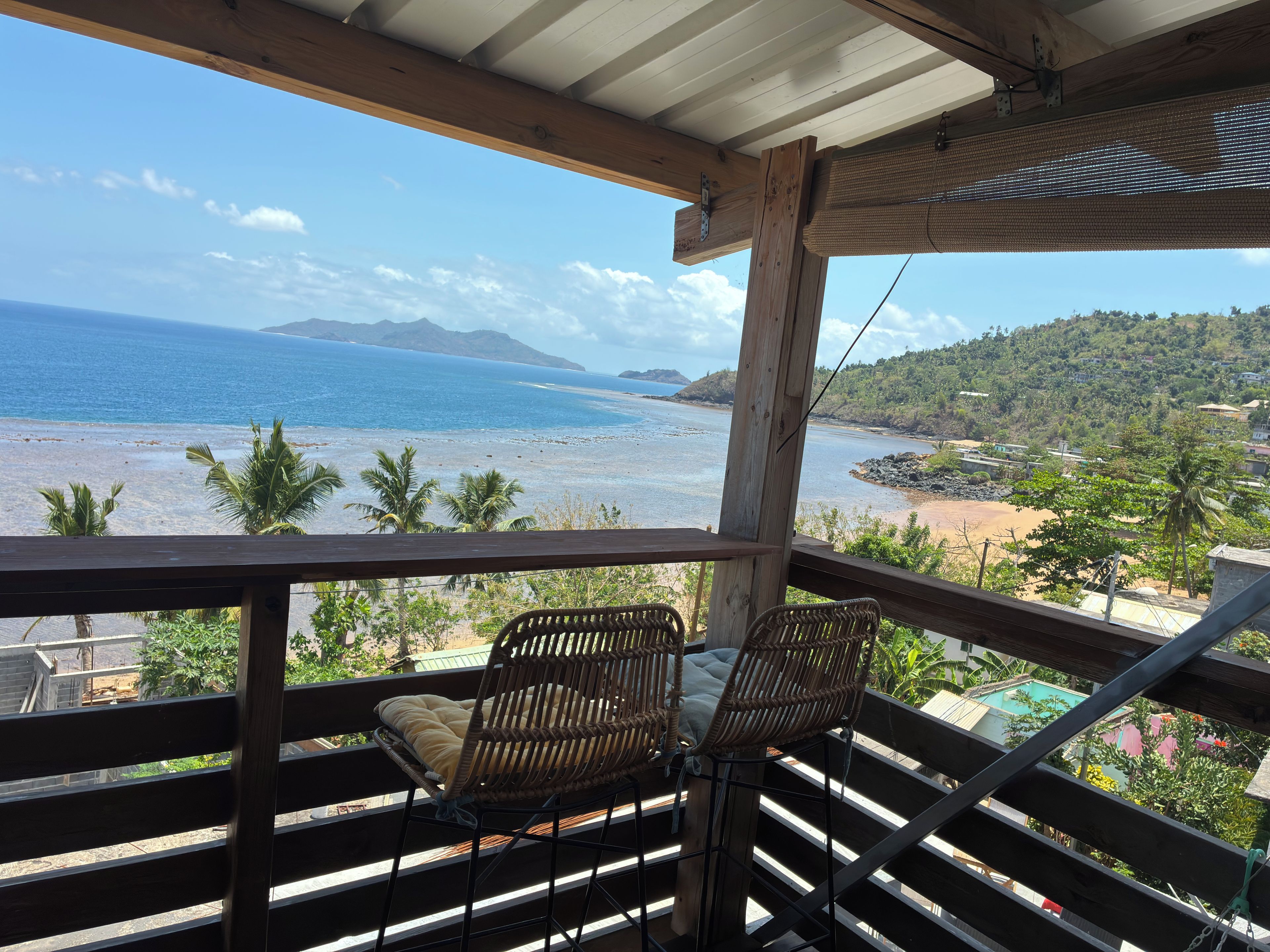 A wooden balcony with wicker chairs overlooking a beach and ocean.