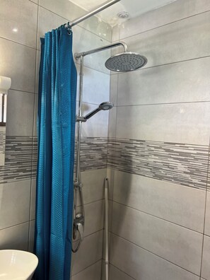 Un'area doccia con soffione a mano, soffione a pioggia montato a parete e tenda da doccia blu.